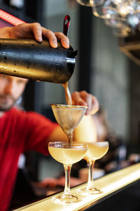 Focused cropped unrecognizable bartender pouring cold refreshing cocktail through strainer in glass placed on counter in bar