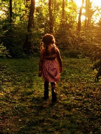 Rear view full length of girl walking on grassy field during sunset