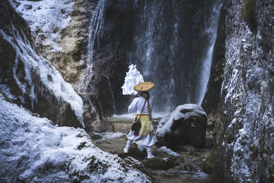 Side view of man standing on rock against waterfall