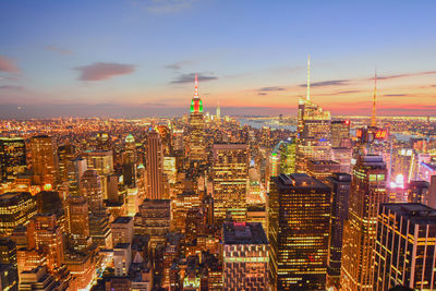 Illuminated empire state building amidst towers at sunset