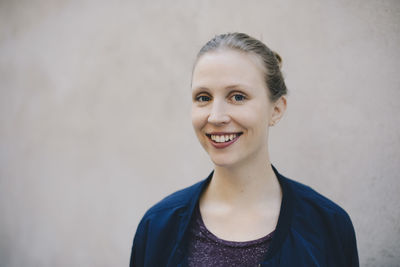 Portrait of happy female computer programmer against beige wall in office