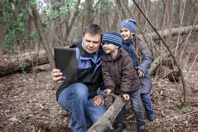 Smiling kids with father talking on video call in forest