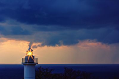 Lighthouse by sea against sky during sunset