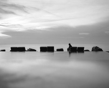 Silhouette person sitting by infinity pool against sky