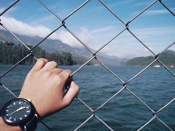 Cropped hand holding chainlink fence against river