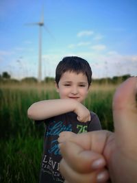 Close-up of person showing thumbs up with boy in background on field 