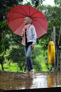 Full length of fashionable woman looking away while standing with umbrella on wet street during rainy season