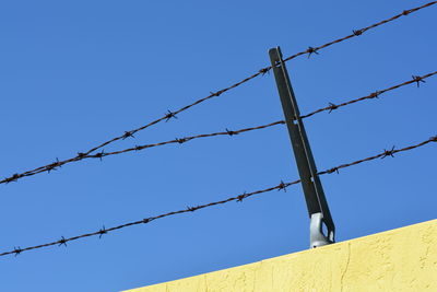 Low angle view of barbed wire fence against clear blue sky