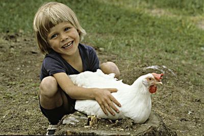 Smiling girl playing with chicken while crouching at field