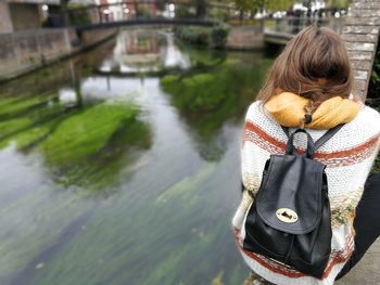 Rear view of woman sitting on retaining wall by river