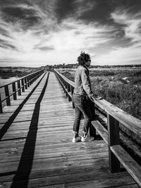 Rear view of woman walking on footpath by footbridge against sky