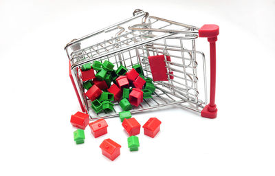 Close-up of toy houses and shopping cart over white background