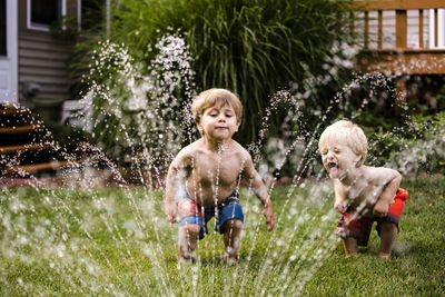 Happy brothers playing with sprinkler in backyard