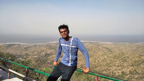 Portrait of smiling man standing on mountain against clear sky