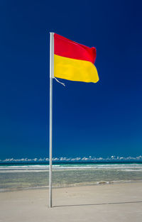 Yellow flag on beach against clear blue sky