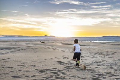 Rear view of boy on beach against sky during sunset