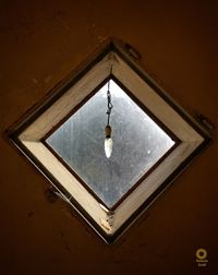 Low angle view of illuminated light bulb hanging on wall