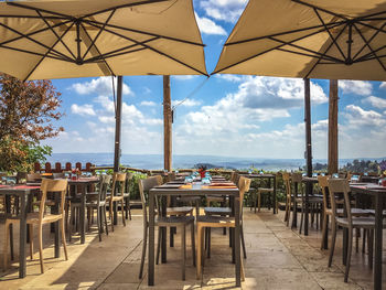 Empty chairs and tables in restaurant against sky