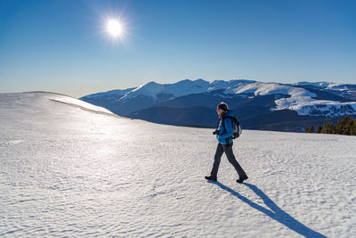 Woman standing on snowcapped mountain against sky on sunny day