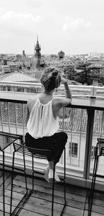 Rear view of woman sitting on chair against sky in city