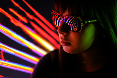 Close-up of girl wearing sunglasses against illuminated light