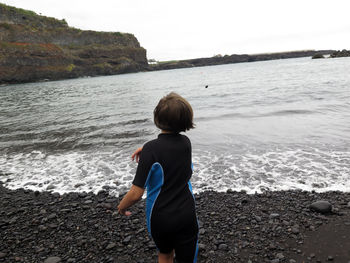 Rear view of girl throwing stones in sea