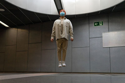 Full body focused asian male wearing casual outfit and face mask levitating with eyes closed above floor in building hallway