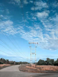 Electricity pylon by road against sky