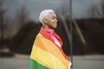 Smiling lgbtqia woman wrapped in rainbow flag