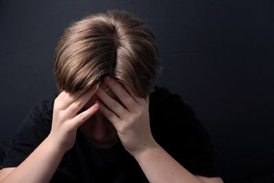 Portrait of teenage girl covering face against black background