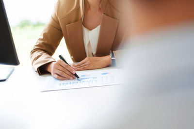 Midsection of businesswoman writing in graph paper at office