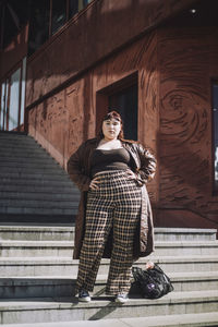 Full length portrait of confident young woman standing with hands on hip during sunny day