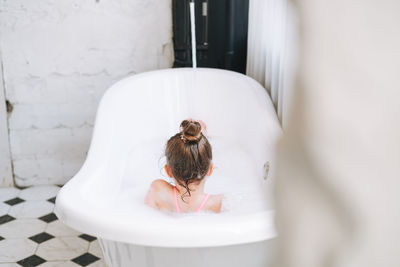 Happy little girl having fun in bath with foam at home