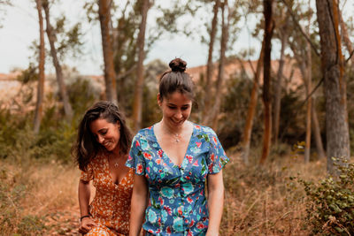 Smiling lesbians walking against tress in forest