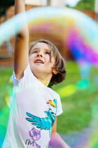 Girl with hand raised standing at park seen through bubble