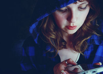 Close-up of mid adult woman wearing blue hooded jacket using smart phone