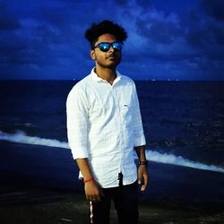 Young man wearing sunglasses standing by sea against sky