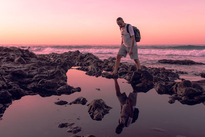 Woman standing on rock at beach against sky during sunset