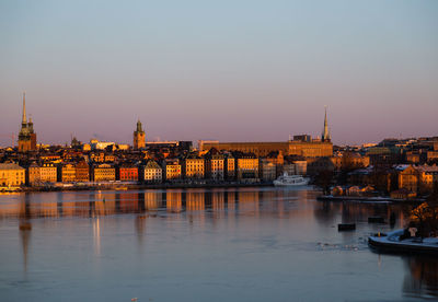 Bridge over river by buildings against sky during sunset