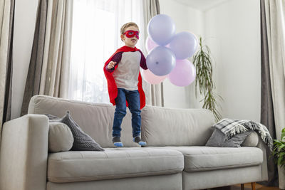 Full length of woman with balloons while sitting on sofa at home
