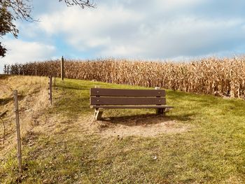 Empty bench on field against sky