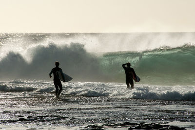 Men with surfboard standing by waves in sea