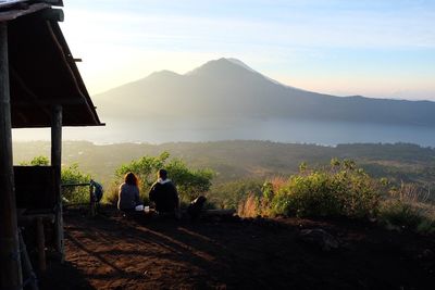 Rear view of man and woman sitting against mount batur during sunrise