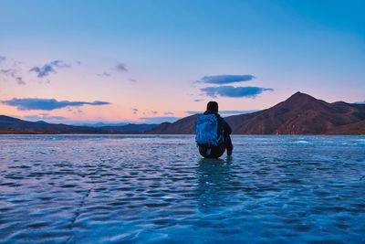 Rear view of man sitting at the beach against sky