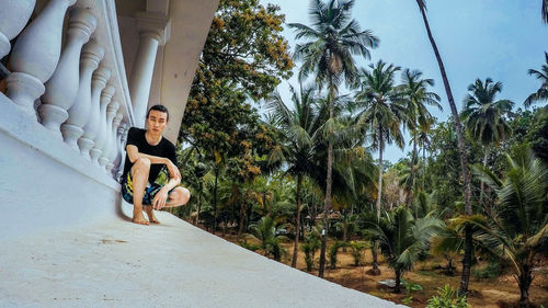 Full length of young man crouching by railing against trees