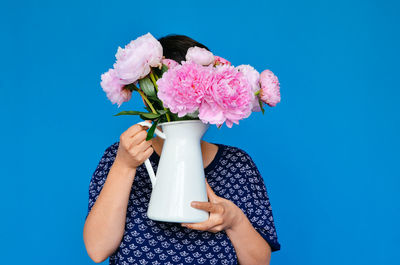 Woman holding pink roses vase in front of face against blue background