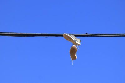 Low angle view of shoes hanging on cables against clear blue sky