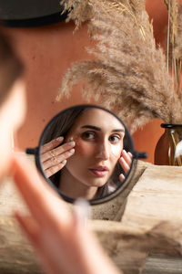 Mirror reflection of woman applying under-eye patch at dressing table closeup