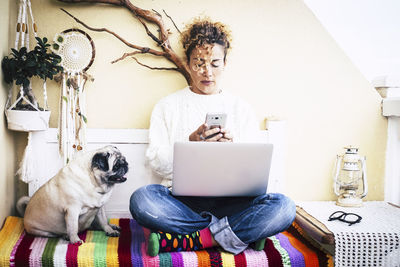 Full length of woman using smart phone while sitting with dog at home