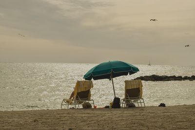 Lounge chairs on beach against a sunset sky